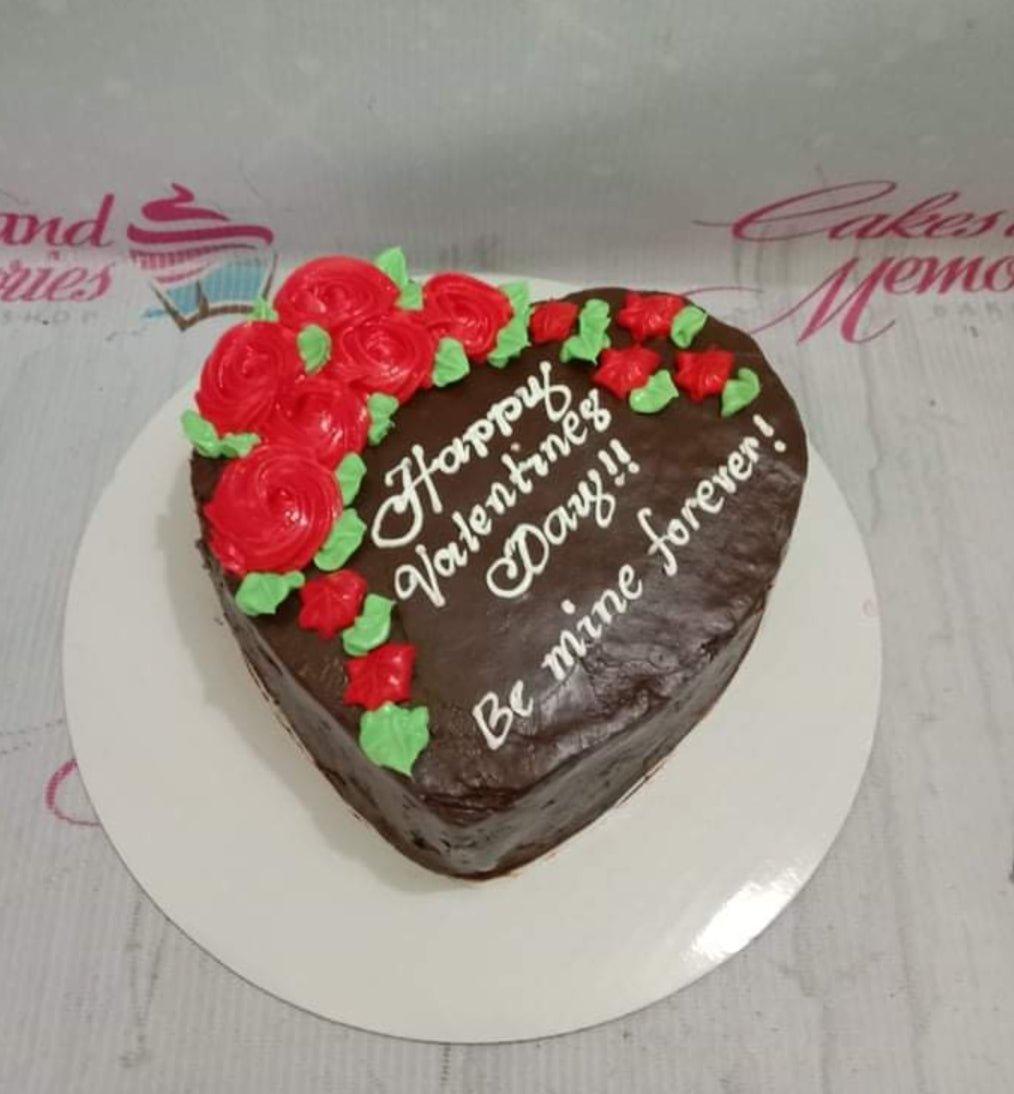 Heart-shaped chocolate cake with red icing roses and white piped message for Valentine's Day.
