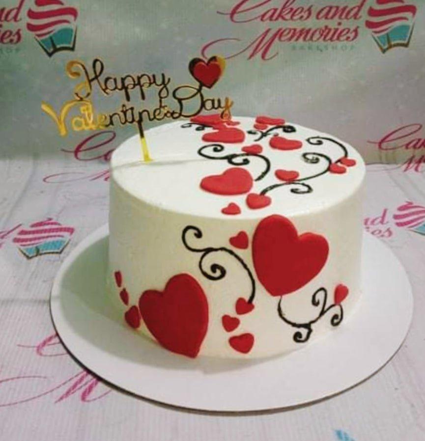 White round cake decorated with red fondant hearts and black icing swirls for Valentine's Day.