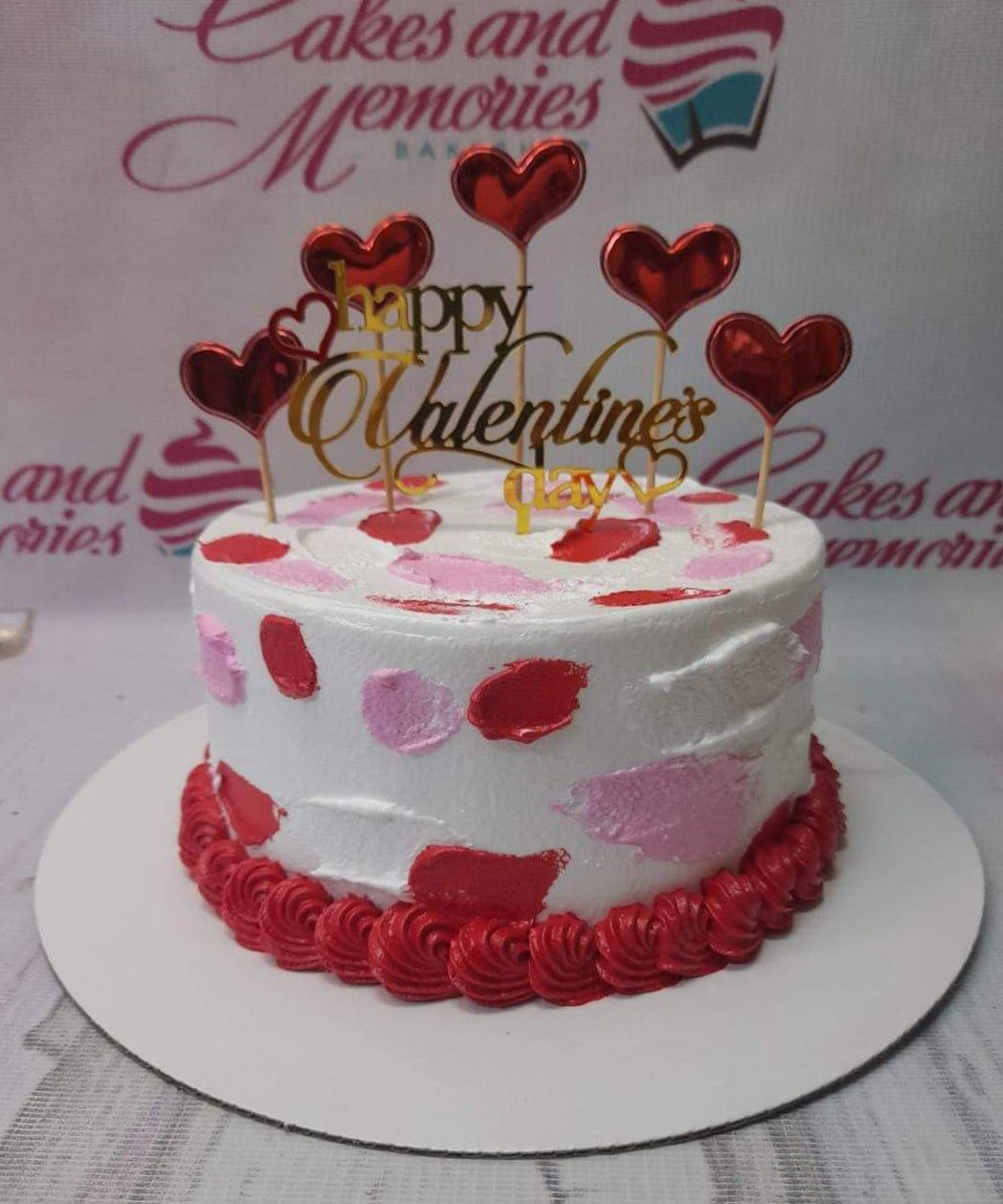 White minimalist Valentine's Day cake with red and pink palette knife icing strokes, red icing base border, and gold heart toppers.
