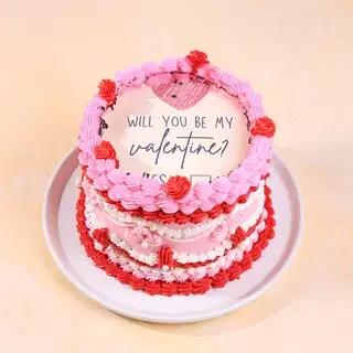 Pink and red vintage-style Valentine's Day cake with piped icing ruffles and a printed message topper.