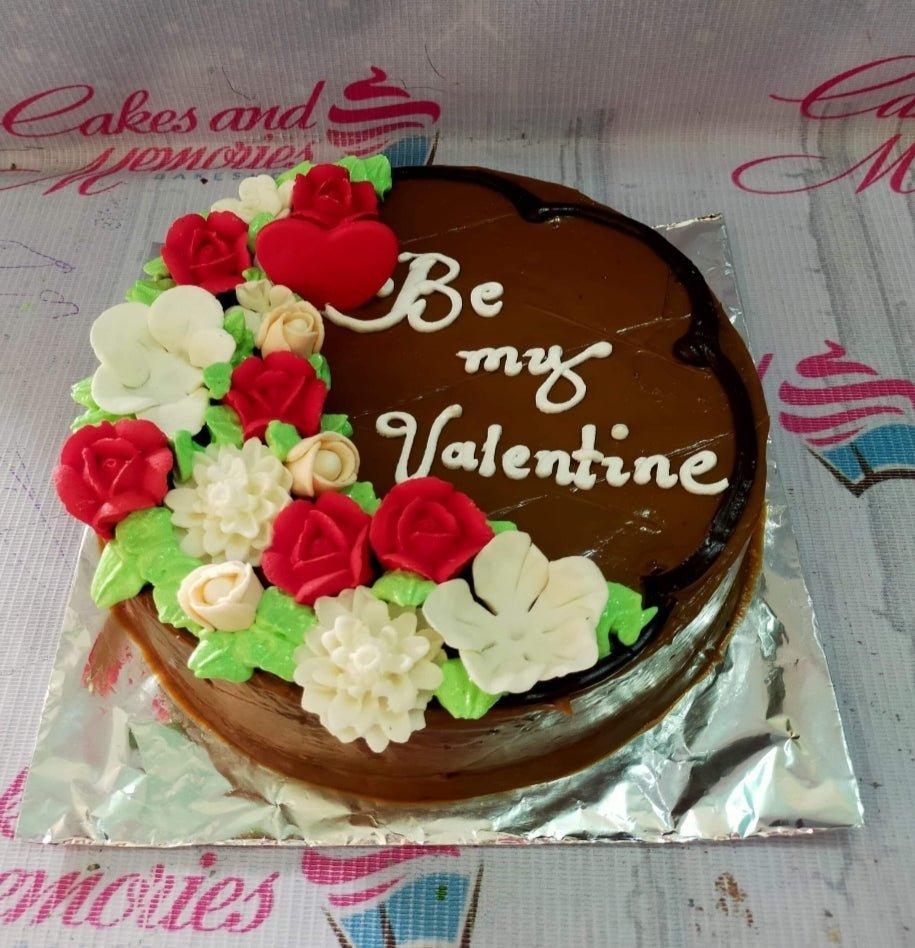 Chocolate cake with red and white fondant flowers and a red heart topper featuring a Be My Valentine message.