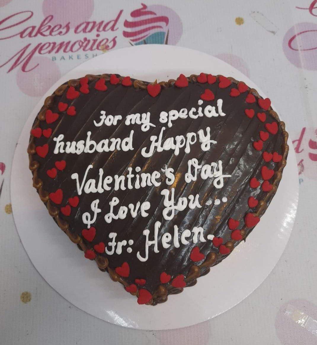 Heart-shaped chocolate cake with red heart decorations and white icing message for a husband's Valentine's Day.