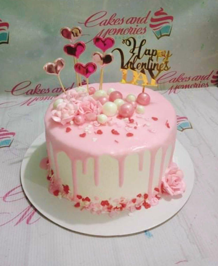 Pink Valentine's Day cake with pink icing drip, heart toppers, and pink roses.