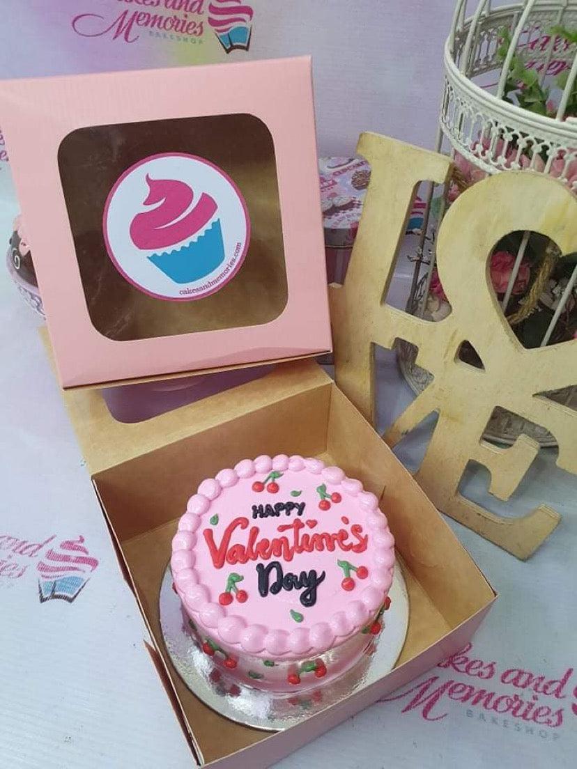 Pink bento cake with piped icing borders, red cherry decorations, and a Happy Valentine's Day message in red and black icing.