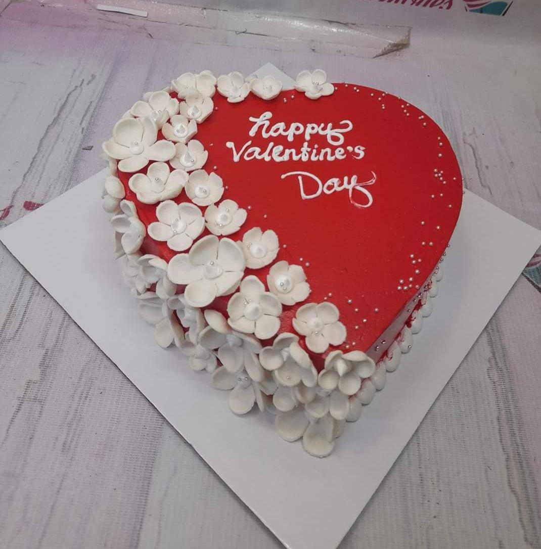 Heart-shaped red Valentine's Day cake decorated with white gumpaste flowers and silver pearls.