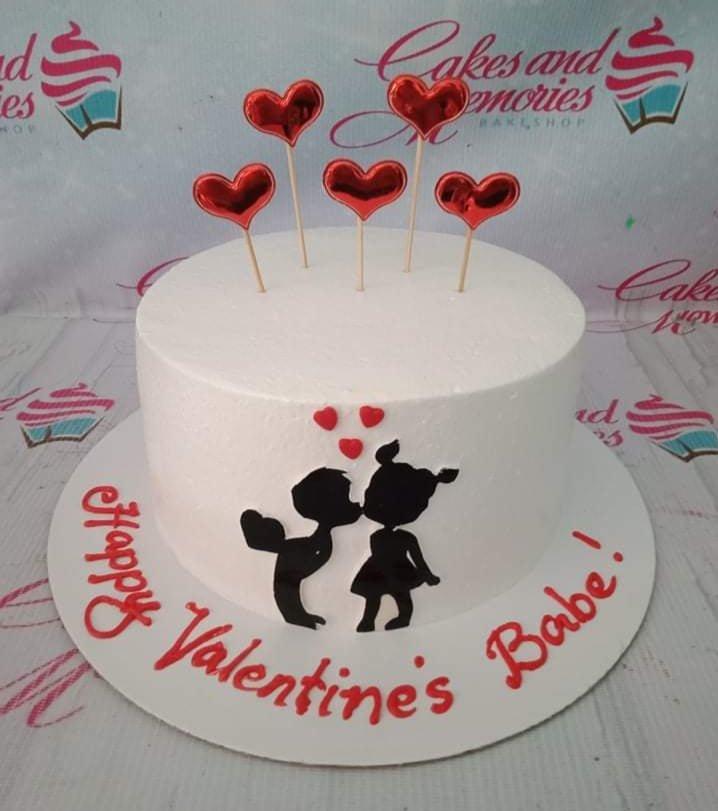 White minimalist Valentine's cake with red heart toppers and a black silhouette of a kissing couple.