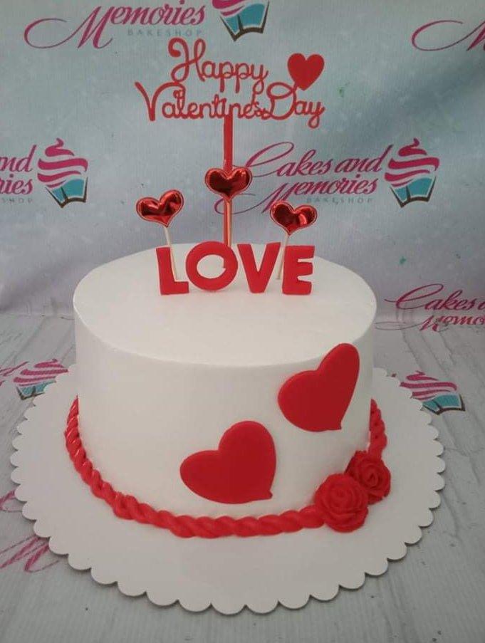 White minimalist Valentine's Day cake with red heart decorations and a Happy Valentine's Day topper.