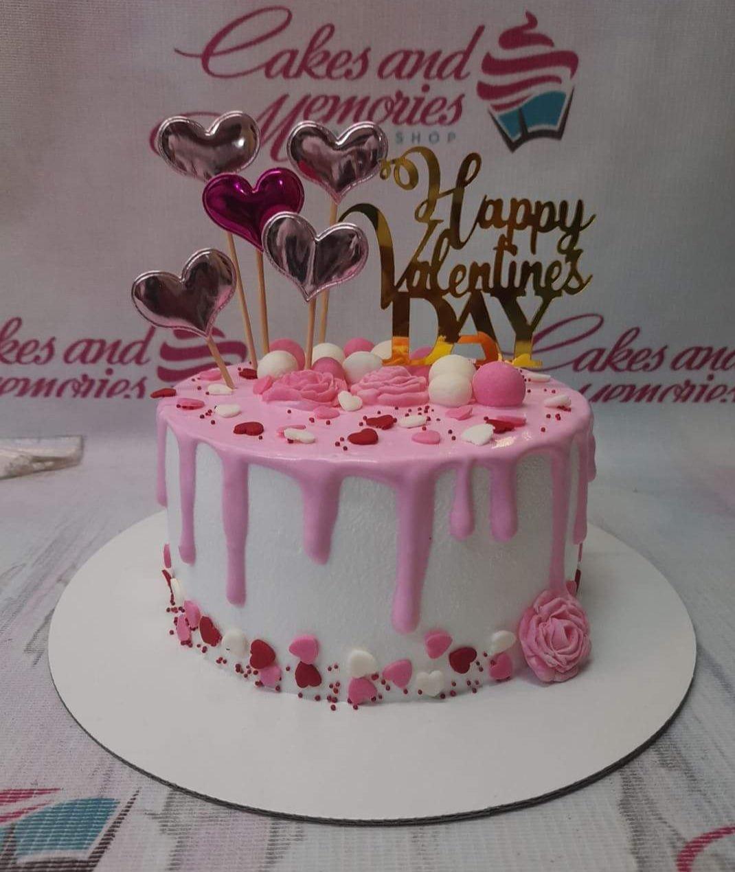 White soft icing cake with pink drip, pink fondant roses, and heart toppers for Valentine's Day.