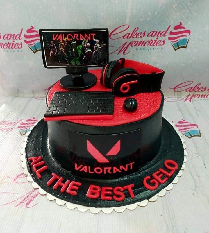 Black and red Valorant themed cake with fondant gaming peripherals including a monitor, keyboard, mouse, and headset.