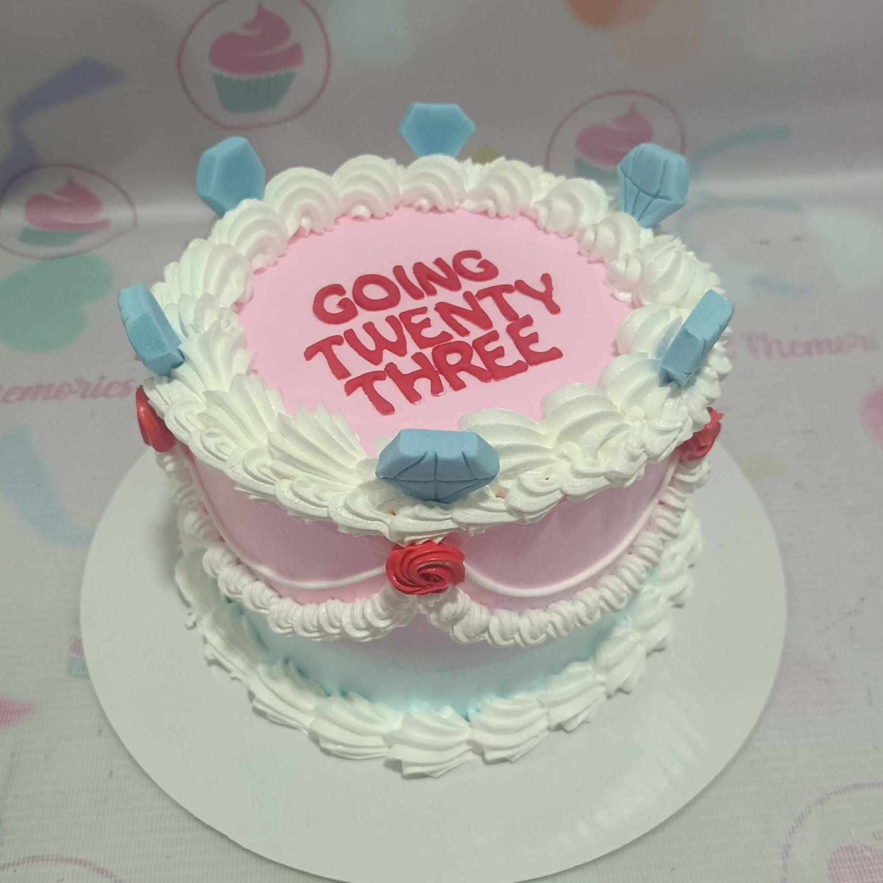 Pink and light blue vintage-style cake with white icing ruffles, red roses, and blue diamond toppers.