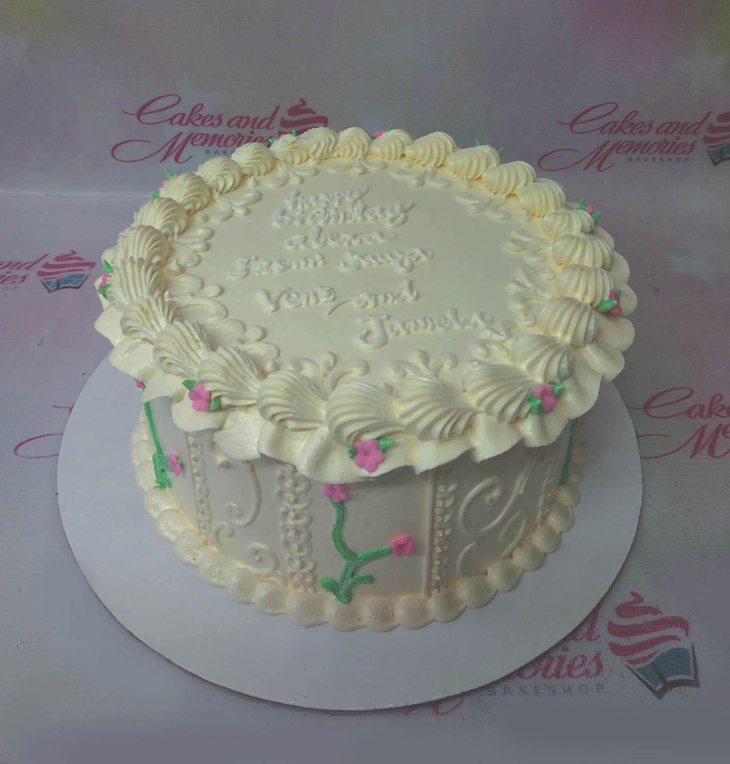 Vintage-style white soft icing cake with piped shell borders, pink floral accents, and a personalized birthday message.