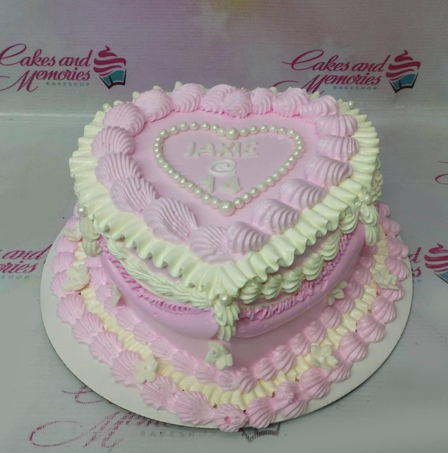 Heart-shaped pink and white vintage lambeth cake with intricate icing ruffles, pearls, and a personalized message for a 14th birthday.