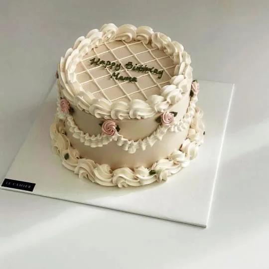 Elegant beige vintage-style birthday cake with white icing ruffles, pink rosettes, and a quilted top pattern.