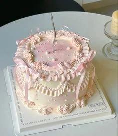 Vintage-style pink and white ruffled cake with delicate icing swags, pink ribbons, and a single tall silver candle.