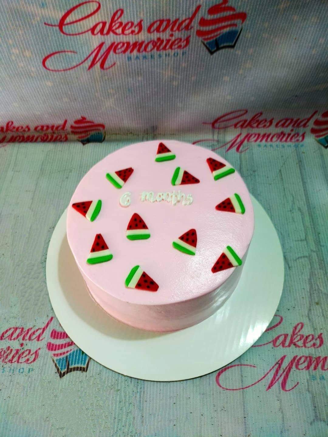 Pink bento cake with watermelon fondant slices and '6 months' message in white icing.