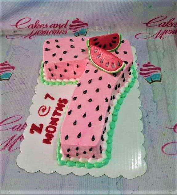 Watermelon themed number 7 shaped cake with pink icing, black seed accents, and fondant watermelon slices.
