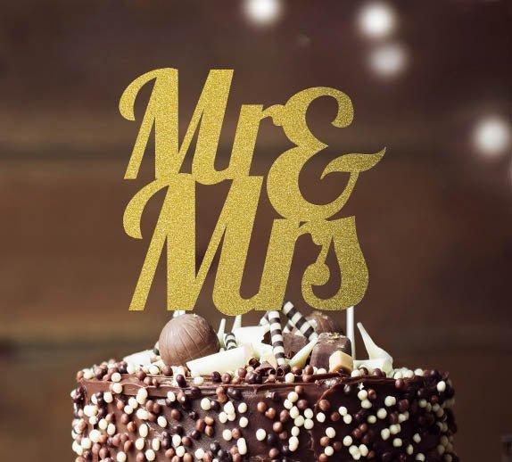 Chocolate cake with dark chocolate icing, white and brown sprinkles, and a gold glitter Mr & Mrs topper.
