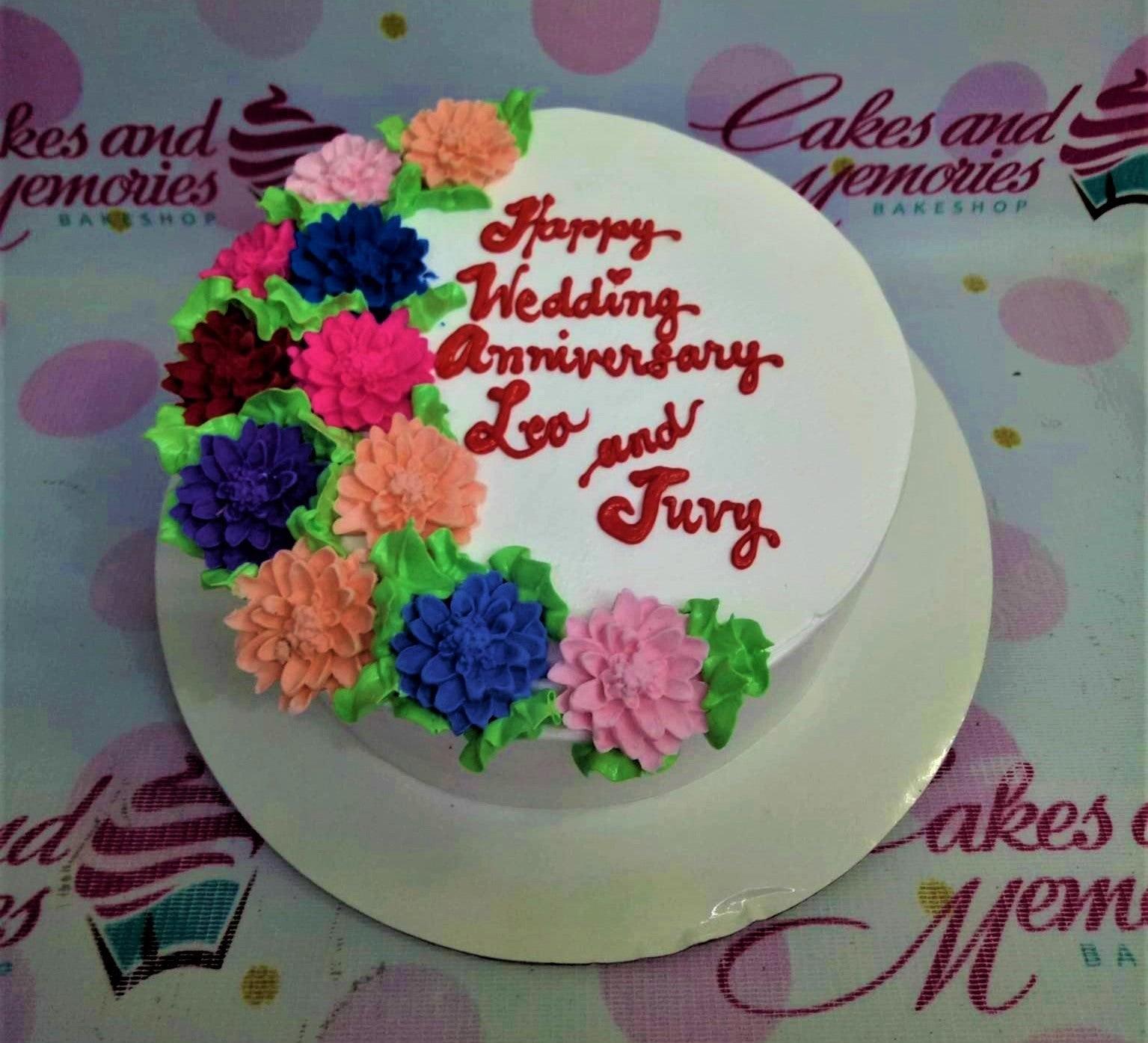 White round anniversary cake with colorful piped icing flowers and red script message
