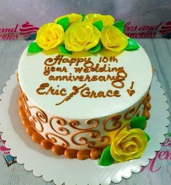 White 1-tier wedding anniversary cake with yellow gumpaste roses, green leaves, and brown icing swirls.