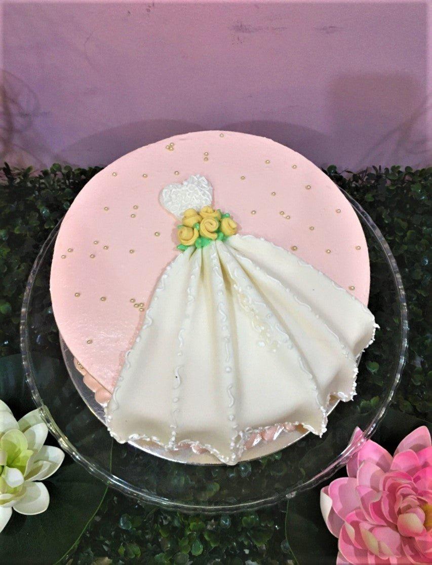Pink minimalist cake featuring a white fondant wedding dress design with yellow roses and gold pearl sprinkles.