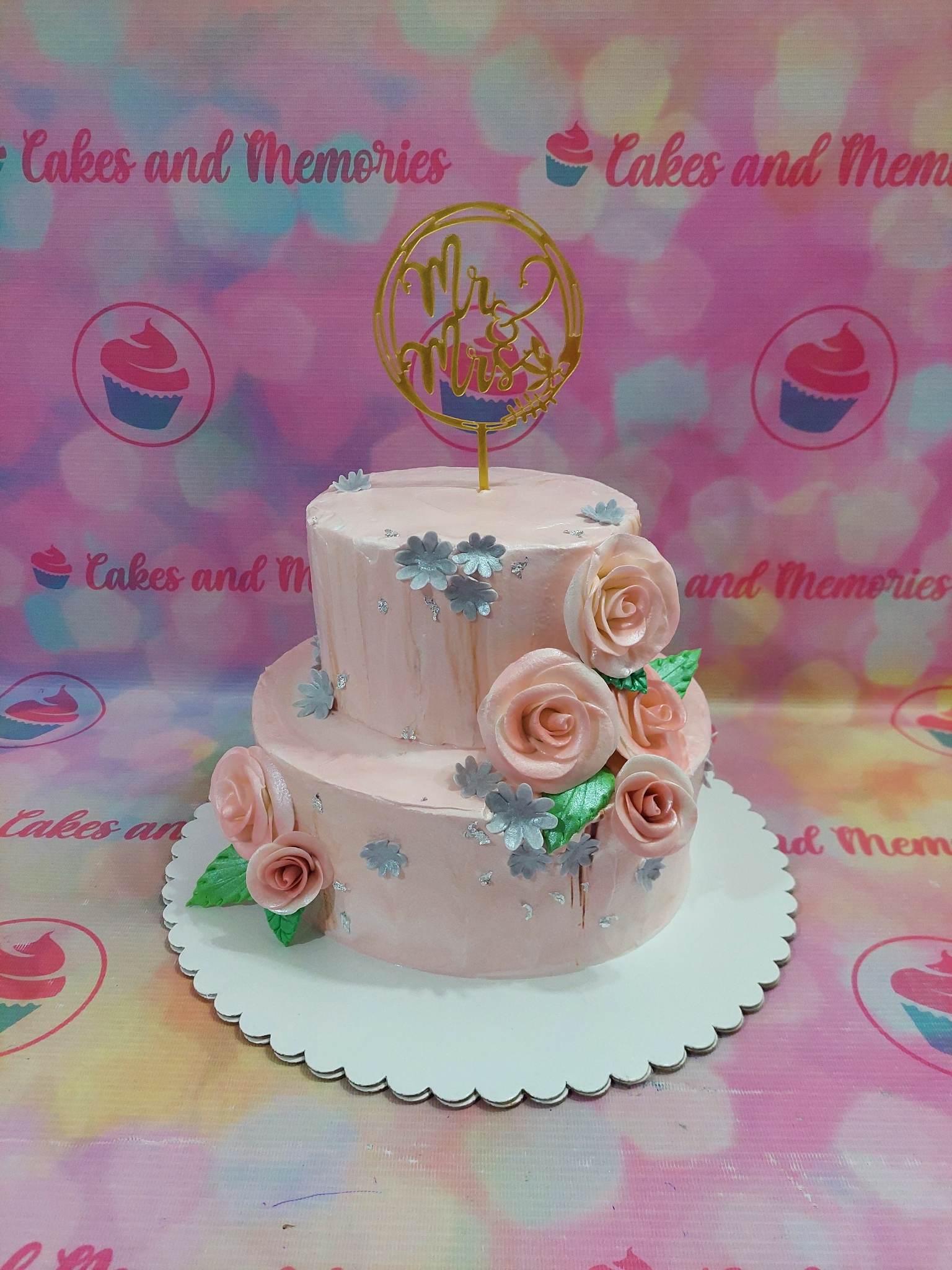 Elegant 2-tier light pink wedding cake with pink gumpaste roses, silver flowers, and a gold Mr & Mrs topper.