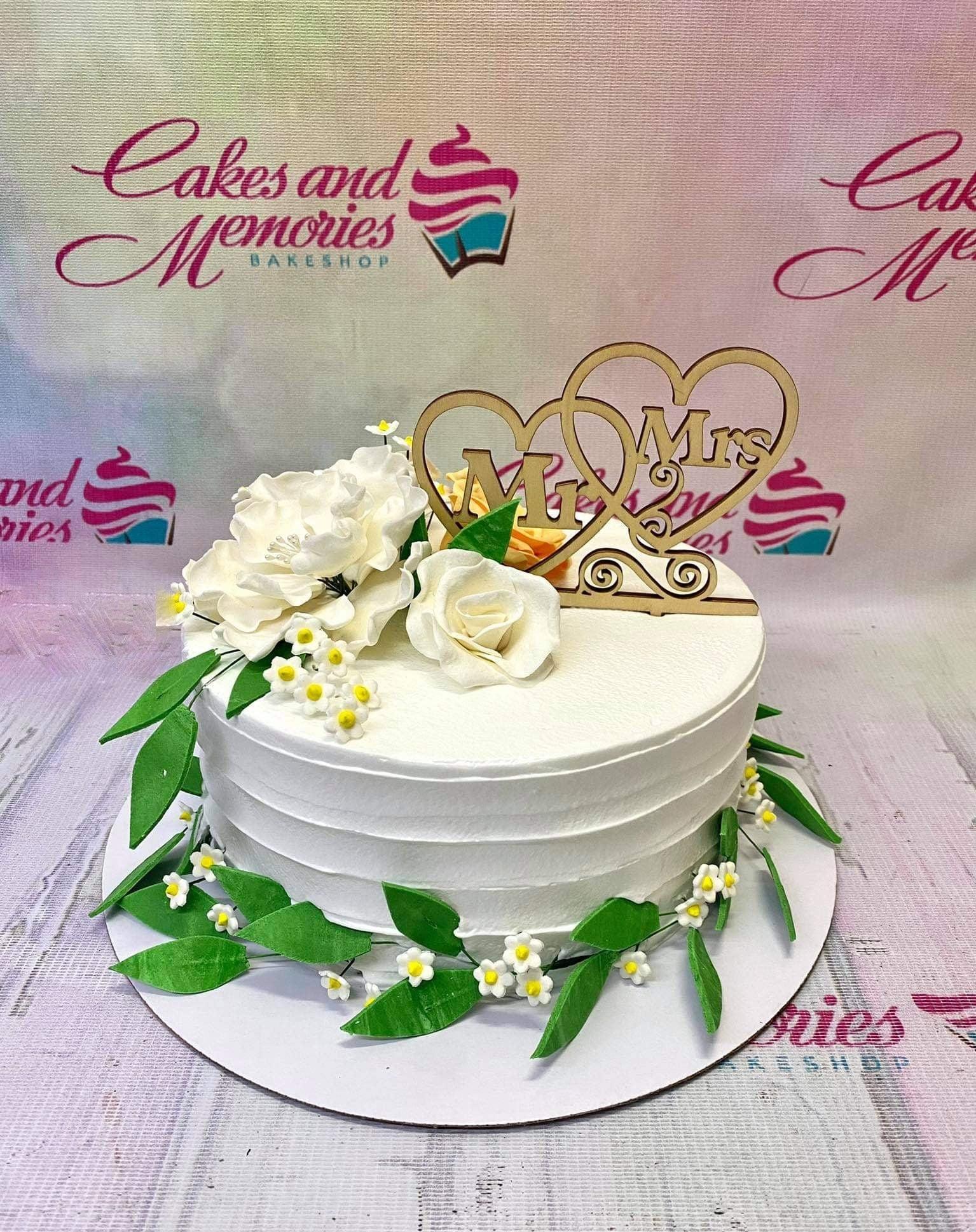 White 1-tier wedding cake with white and peach gumpaste flowers, green leaves, and a wooden Mr & Mrs heart topper.
