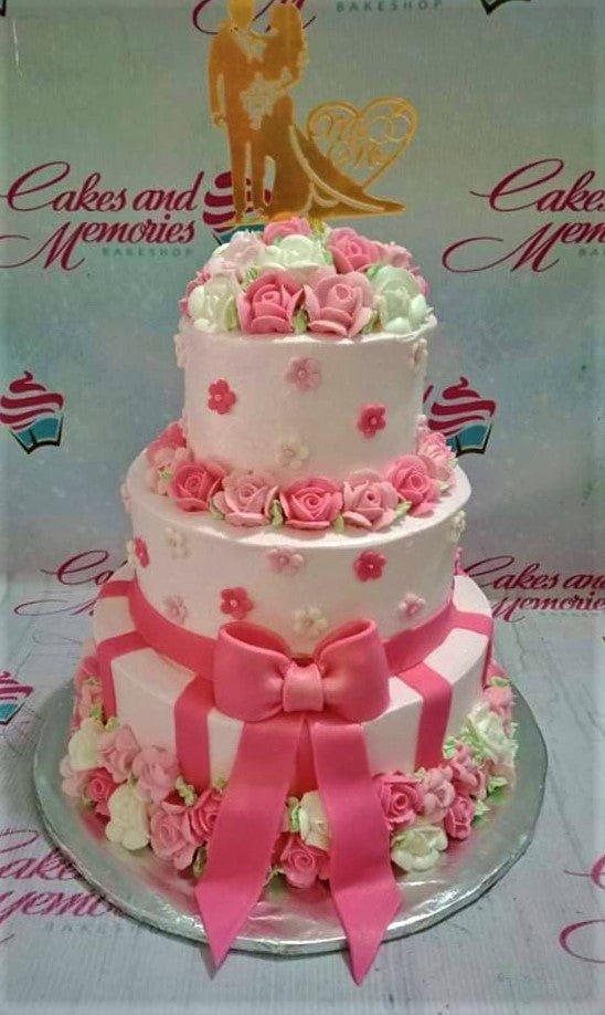 Elegant 3-tier pink and white wedding cake adorned with numerous pink and white icing roses and a gold couple topper.