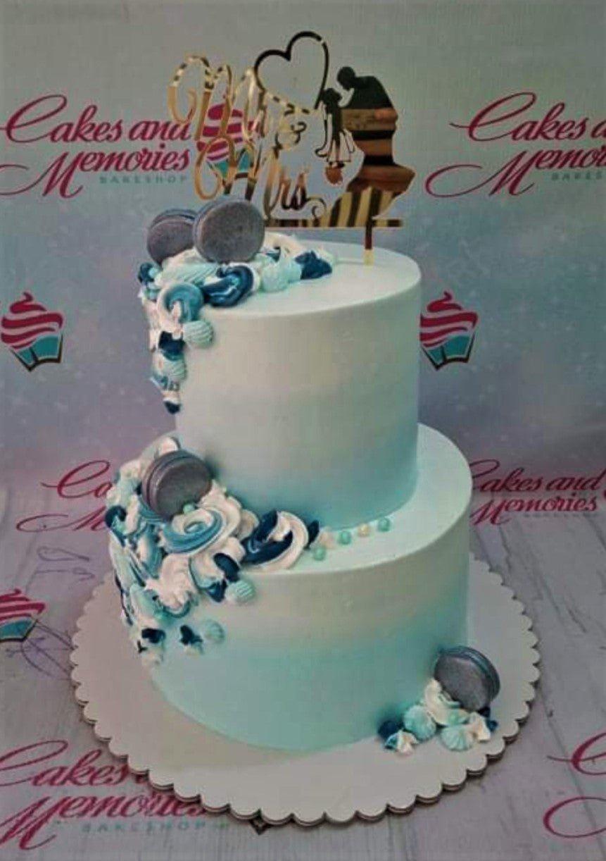 Two-tier light blue ombre wedding cake with a gold Mr & Mrs topper and blue macaron accents.