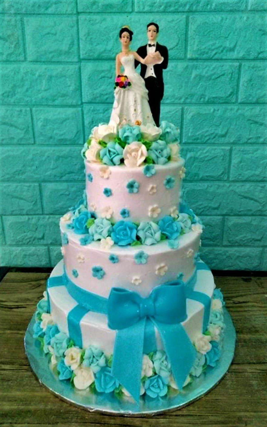 Elegant 3-tier white wedding cake with light blue and white icing roses, a large blue bow, and a bride and groom topper.