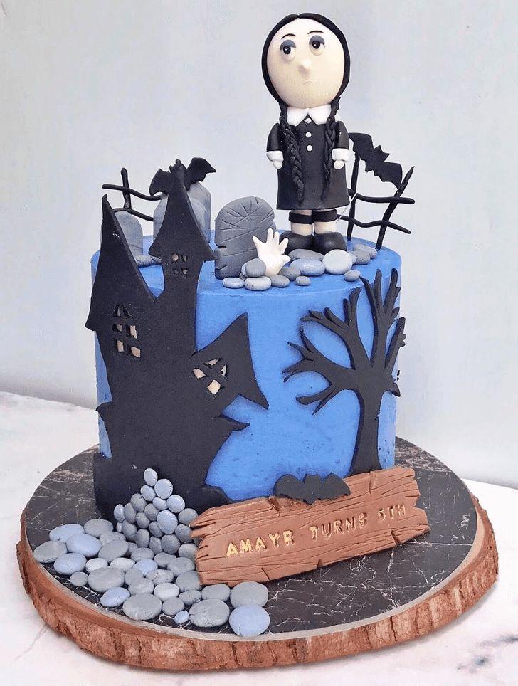 Wednesday Addams themed blue cake with a fondant figure, haunted house silhouette, and a wooden sign message.