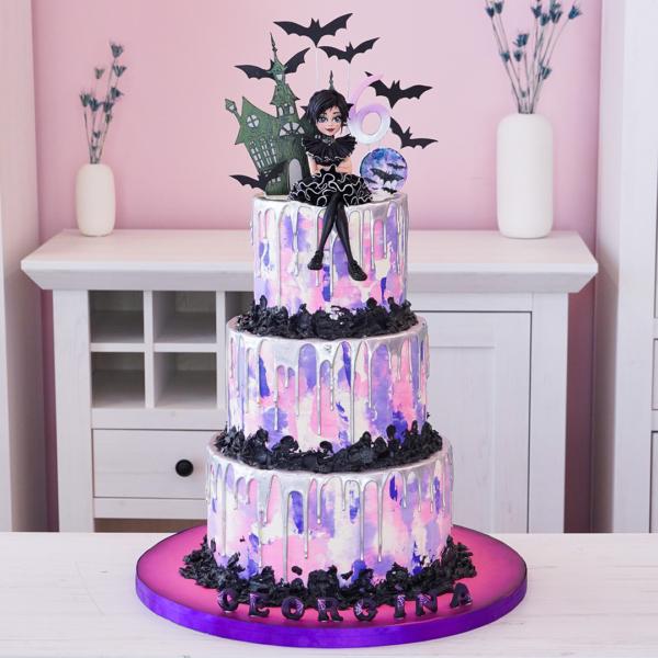 Three-tier Wednesday Addams themed cake with purple, pink, and white marbled icing, silver drips, black ruffles, and character toppers.