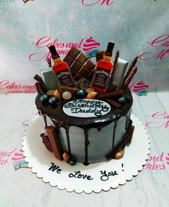 Gray and black whiskey themed birthday cake with chocolate bars, Jack Daniels printouts, and chocolate drip.