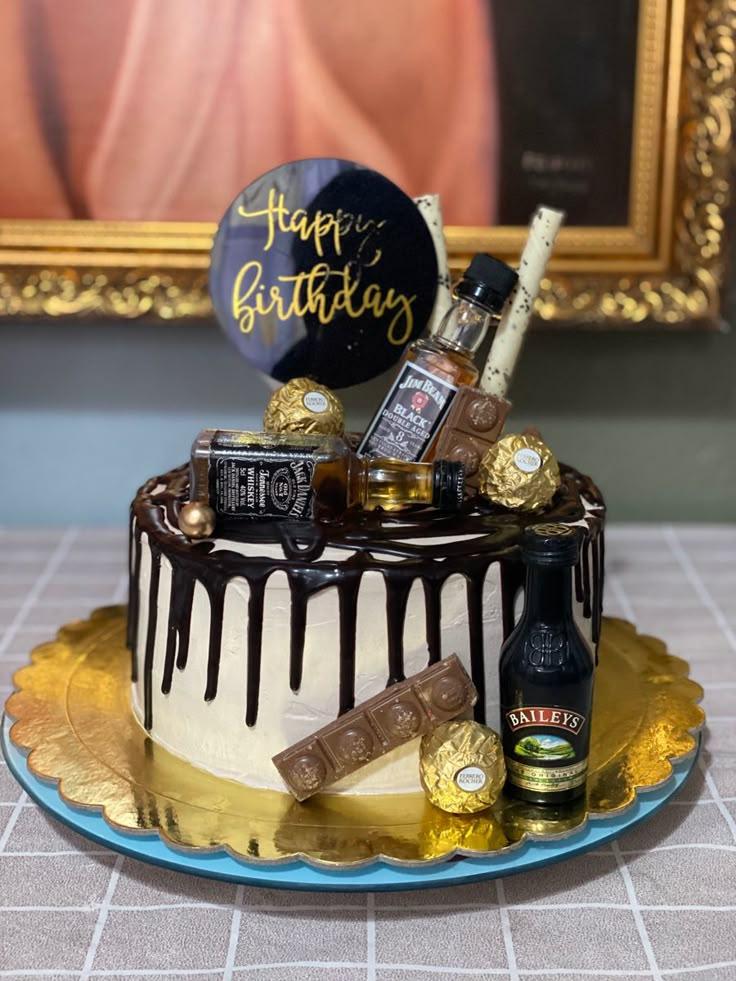 White 1-tier cake with chocolate drip, liquor bottles, Ferrero Rocher chocolates, and a black Happy Birthday topper.