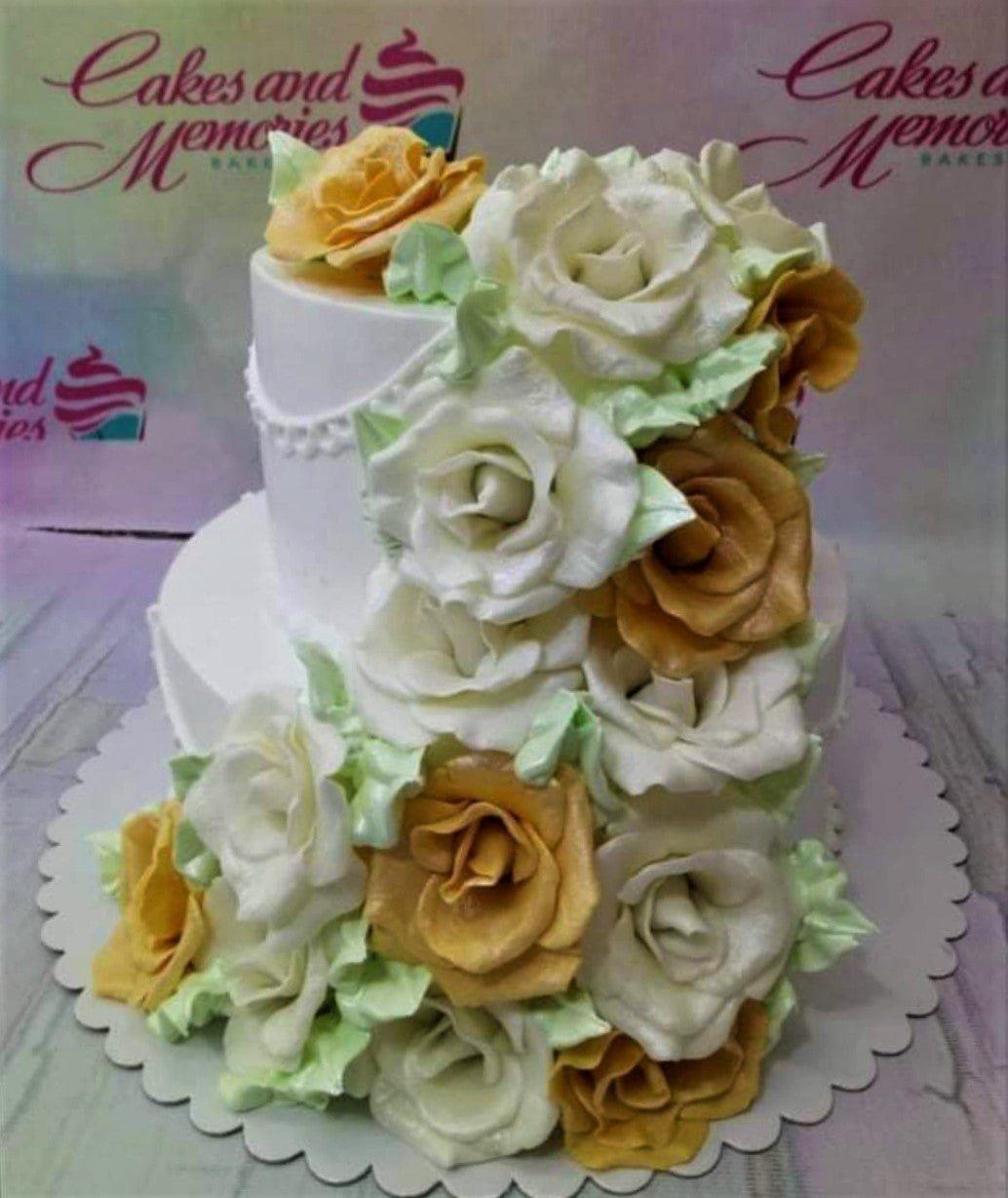 Elegant two-tier white cake adorned with a cascading floral arrangement of white and gold icing roses and light green leaves.