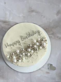 White minimalist birthday cake with silver and white pearl sprinkles and silver Happy Birthday icing text.