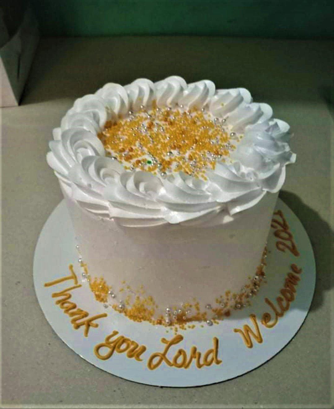 White minimalist cake with gold and silver sprinkles, white icing rosettes, and a gold message on the base board.