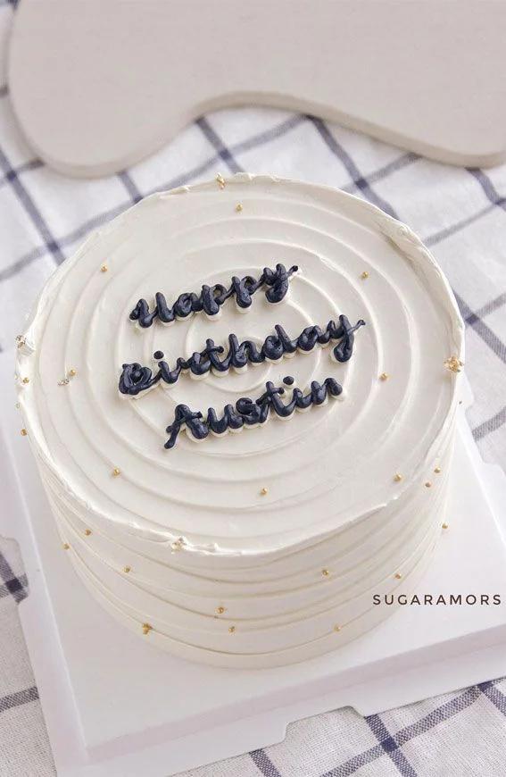 White minimalist birthday cake with spiral textured icing, gold dragees, and navy blue piped message for Austin.