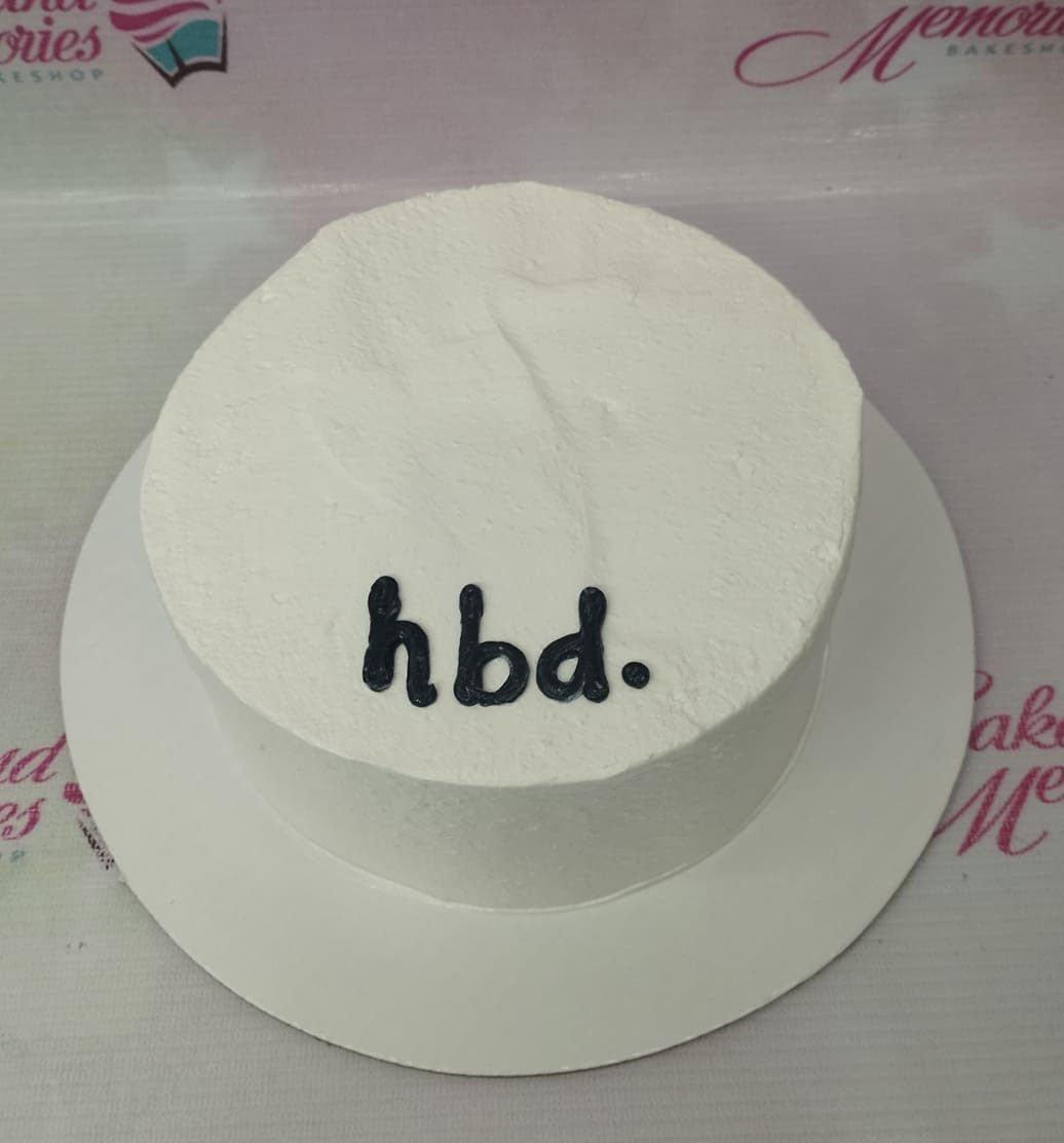 White minimalist bento cake with black piped icing text reading hbd.