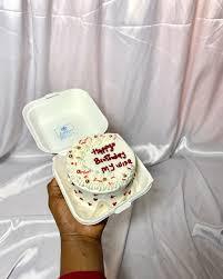 White bento cake with red icing text and colorful sprinkles in a white clamshell box.