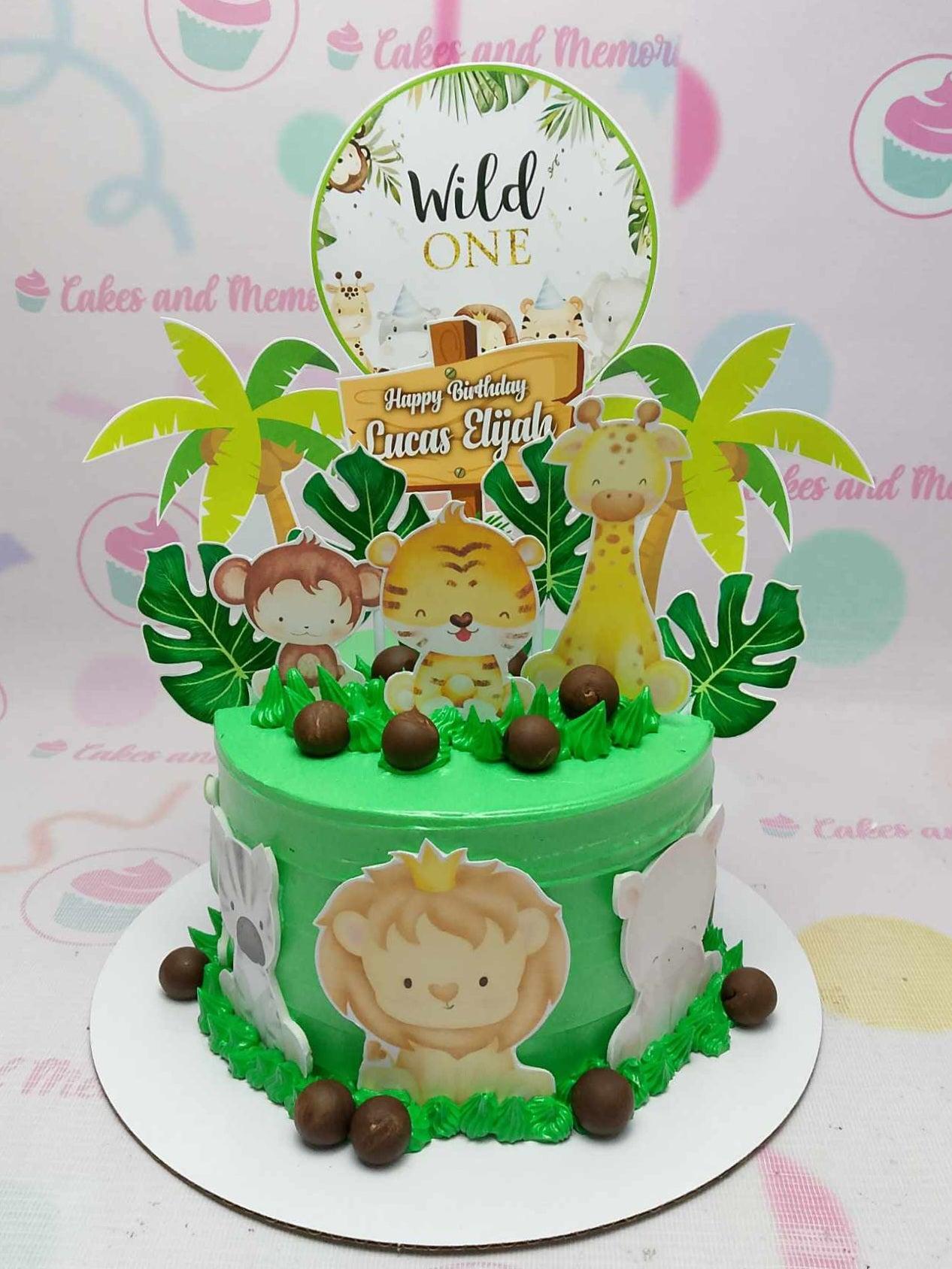 Green jungle safari themed birthday cake with cute animal printouts, palm trees, and chocolate balls for Lucas Elijah's first birthday.