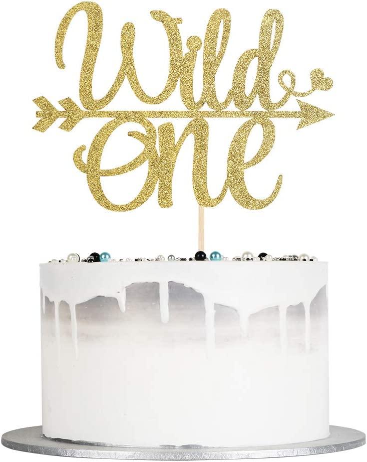 White minimalist cake with a white chocolate drip and a large gold glitter Wild One topper with blue and black pearl sprinkles.