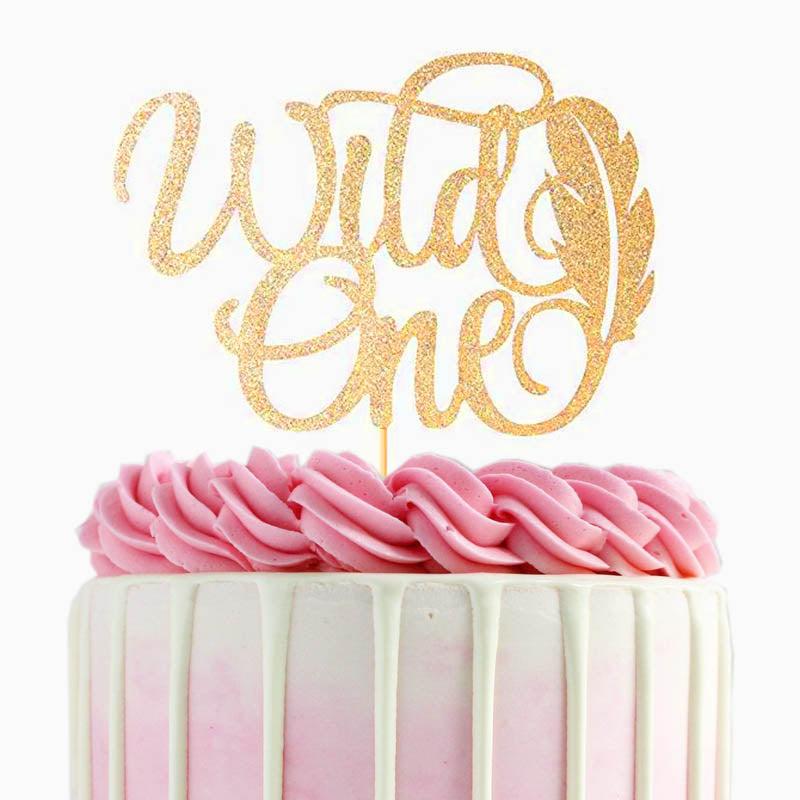 Pink and white ombre cake with white chocolate drip, pink icing rosettes, and a gold glitter Wild One topper.