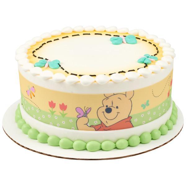 Winnie the Pooh themed birthday cake with yellow and green edible side wrap, white icing borders, and teal butterfly decorations.