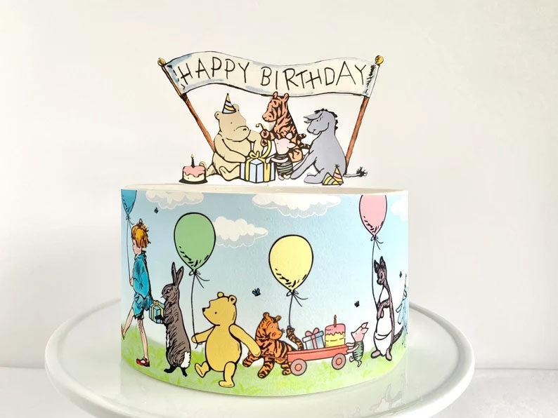 Winnie the Pooh themed birthday cake with a light blue side wrap featuring Christopher Robin and friends with a Happy Birthday banner topper.