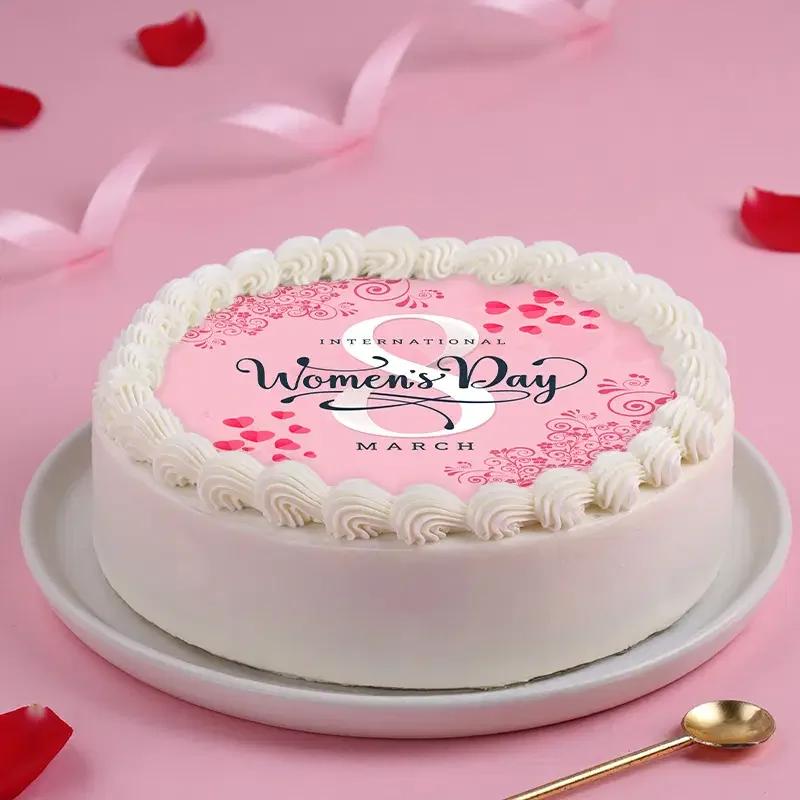 White round cake with pink International Women's Day edible print top and white icing rosettes.