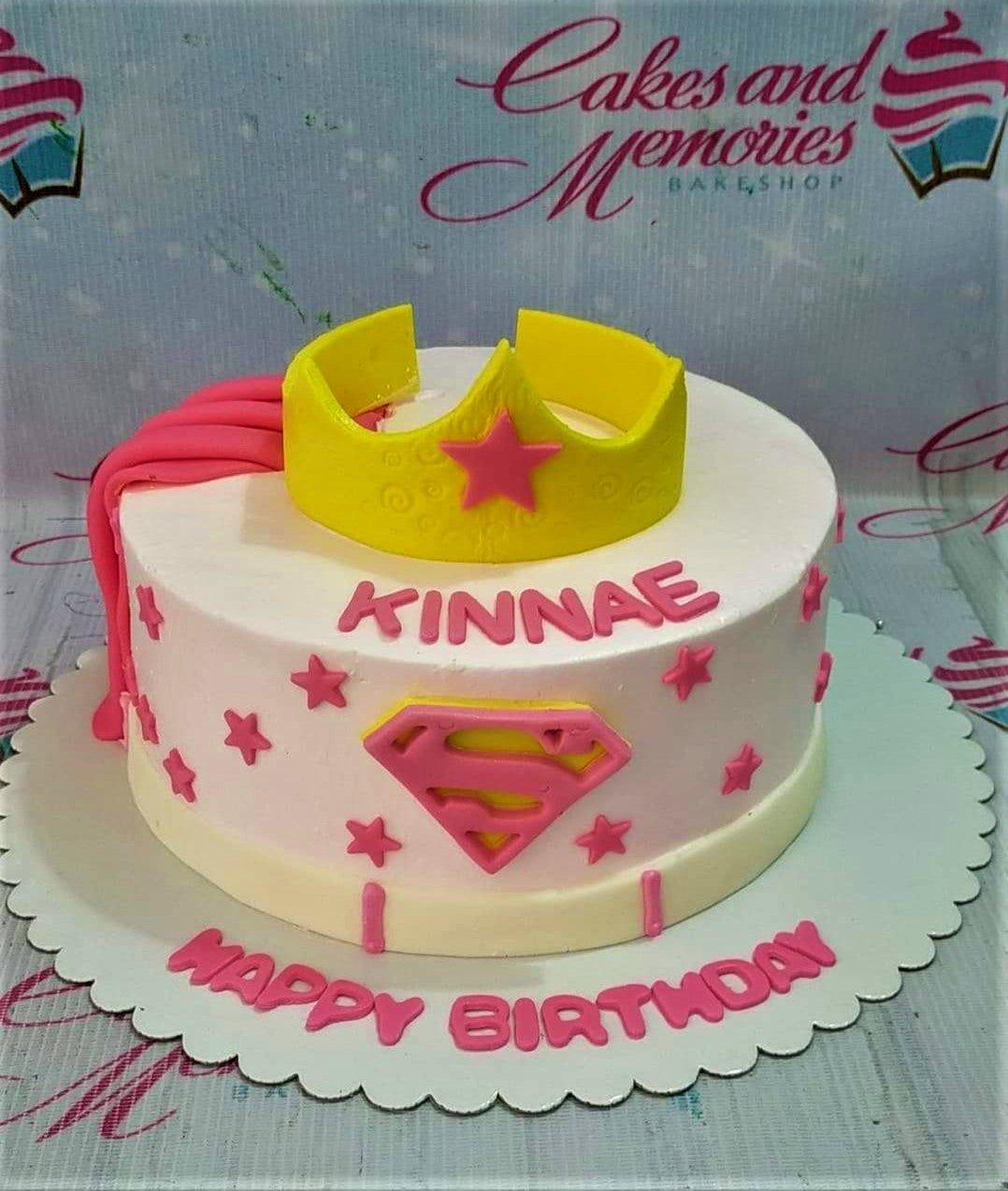 Pink Wonder Woman themed birthday cake with a yellow fondant crown, pink cape, and Superman logo for Kinnae.