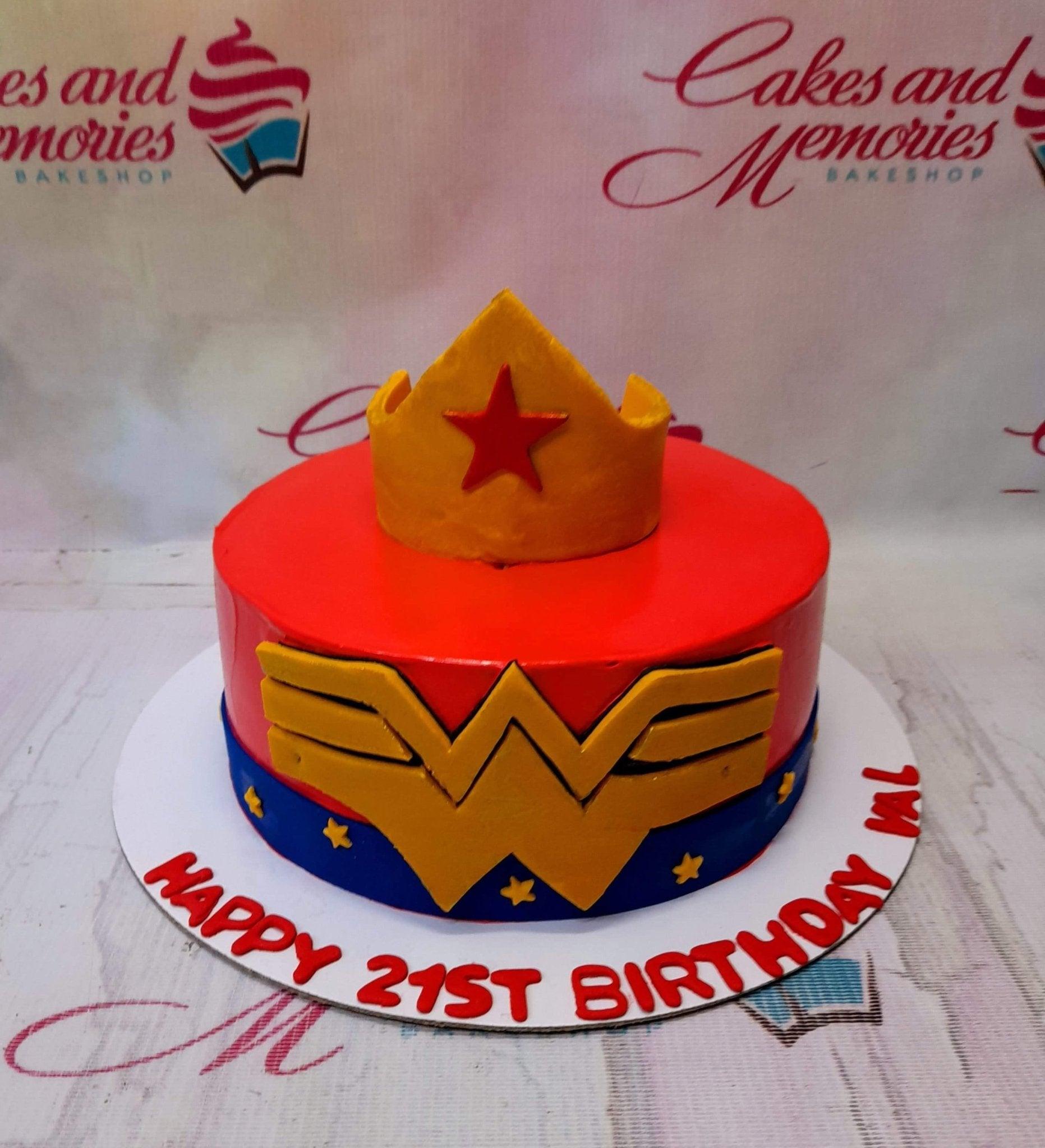Wonder Woman themed red and blue birthday cake with a gold crown topper and the iconic W logo on the side.