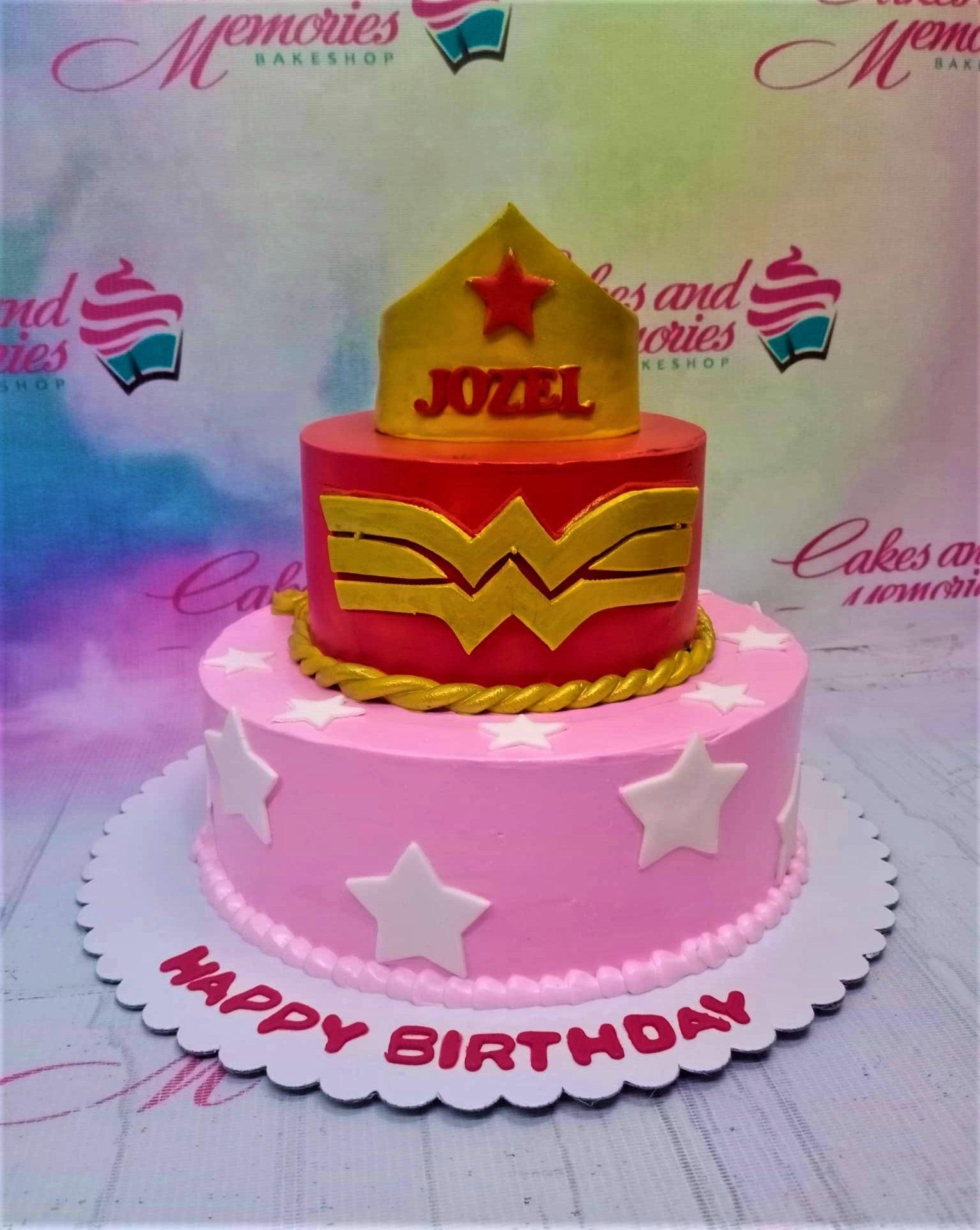 Two-tier Wonder Woman themed birthday cake with a gold crown topper, red and pink icing, and white fondant stars.