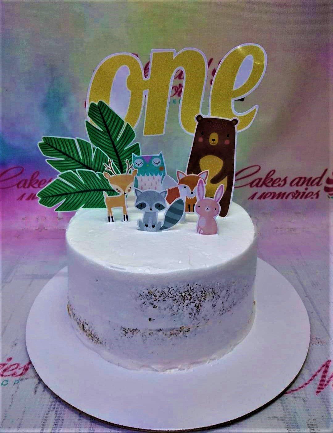 Semi-naked white woodland animal themed birthday cake with a gold glitter 'one' topper and forest animal printouts.