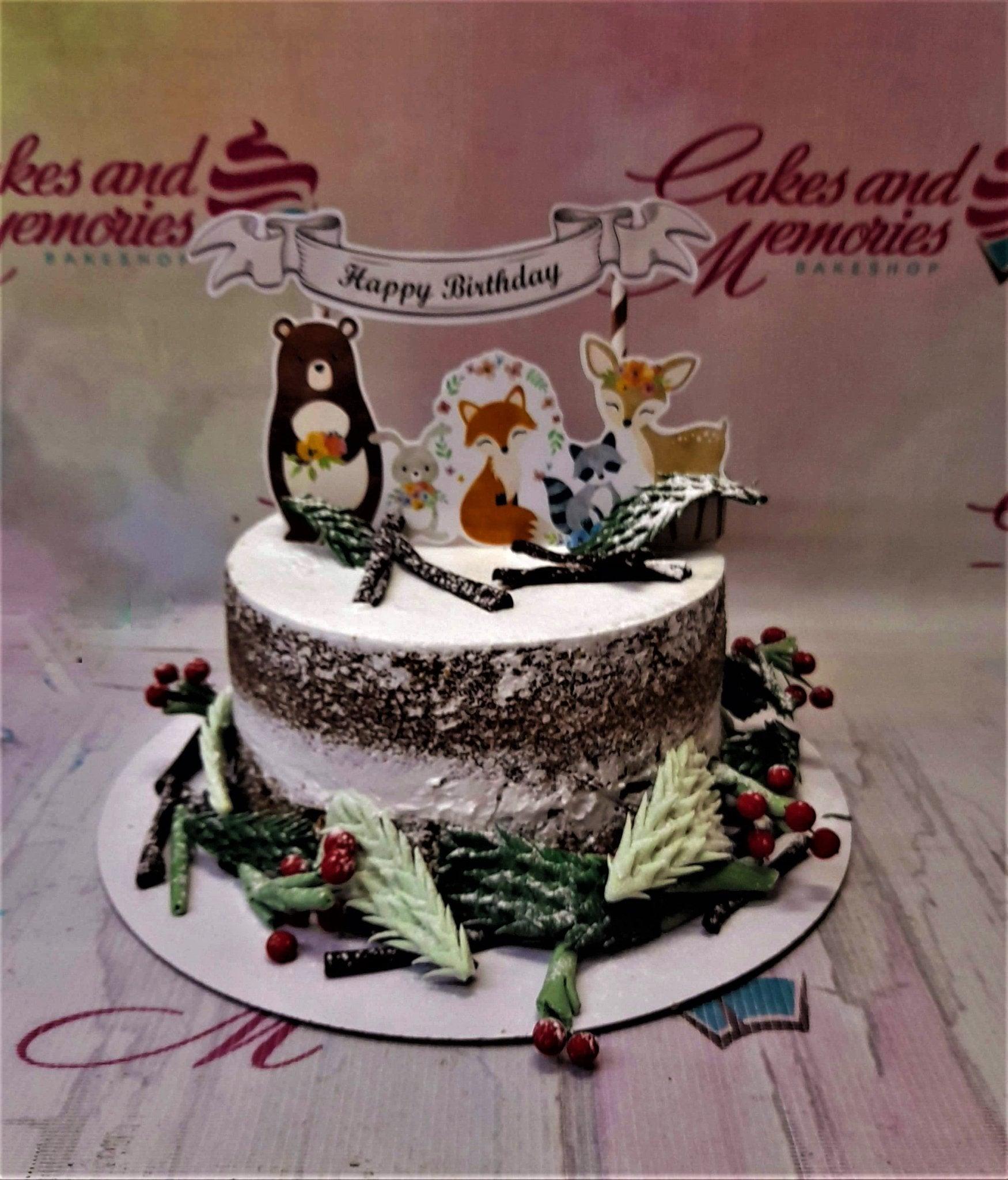 Woodland animal themed birthday cake with a semi-naked icing finish, featuring forest animal printouts and gumpaste pine branches.